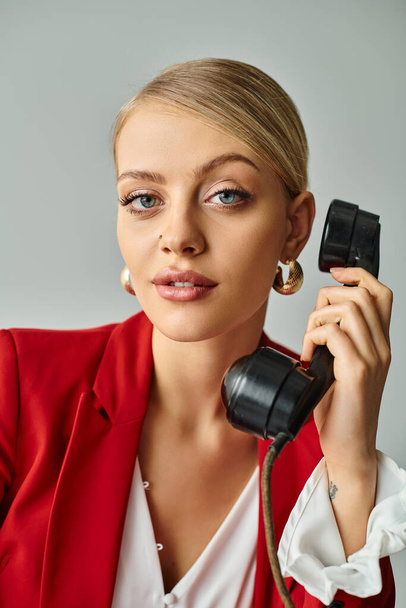 portrait of jolly appealing woman in red jacket talking by vintage phone and looking at camera - Photo, Image