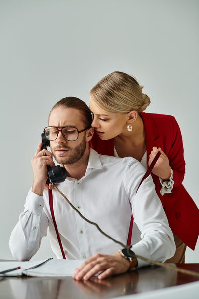 skoncentrowany młody człowiek z brodą rozmawia przez telefon retro podczas jego gorąca dziewczyna uwodzi go - Zdjęcie, obraz