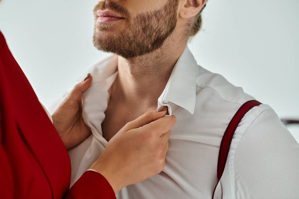 cropped view of young woman in red jacket touching collar of her bearded boss, work affair - Photo, Image