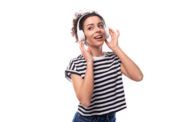 νέα θετική σγουρή μελαχρινή γυναίκα λάτρης της μουσικής σε ένα ριγέ casual t-shirt με ακουστικά χορό. - Φωτογραφία, εικόνα