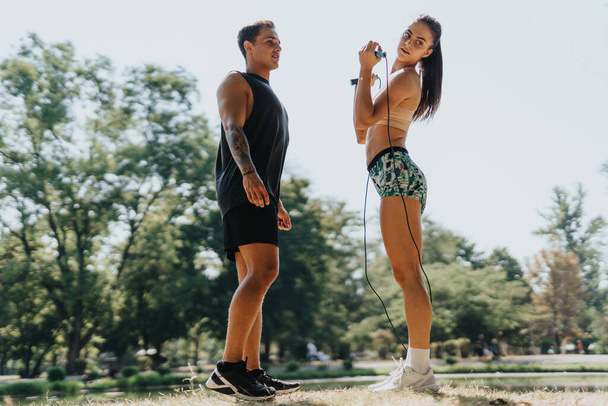 Egy kaukázusi pár ugrókötelezi magát egy parkban, bemutatva a testüket és az egészséges életmód iránti elkötelezettségüket. Bemelegítenek, nyújtózkodnak, és részt vesznek egy kihívásokkal teli edzésen.. - Fotó, kép