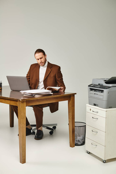 vonzó szakállas férfi barna elegáns kabát dolgozik a laptop és nézi a papírmunka - Fotó, kép