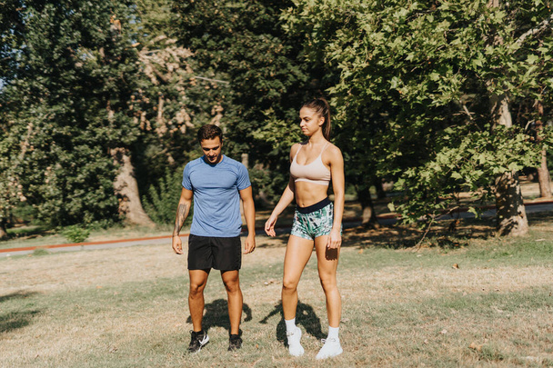 Jovem, casal em forma exercitando ao ar livre em um parque ensolarado. Motivados e persistentes, eles praticam fitness e alongamento, abraçando um estilo de vida saudável.. - Foto, Imagem