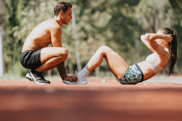 Caucasian athletes enjoy a sunny day in the park as they perform core exercises. Wearing sportswear, they motivate each other during their outdoor workout, using elastic bands for added challenge. - Photo, Image