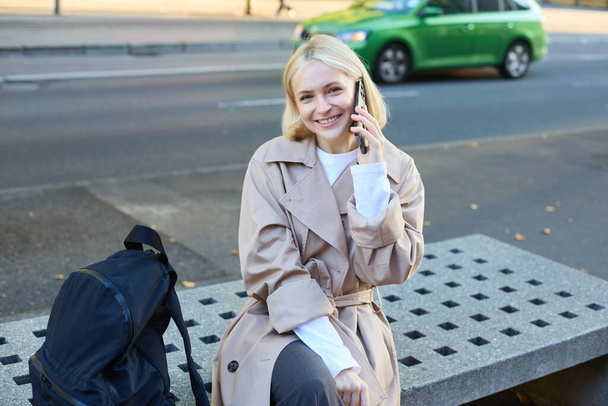 Jeune étudiante mignonne, femme parlant sur un téléphone portable alors qu'elle était assise sur un banc de rue, bavardant sur un smartphone. - Photo, image