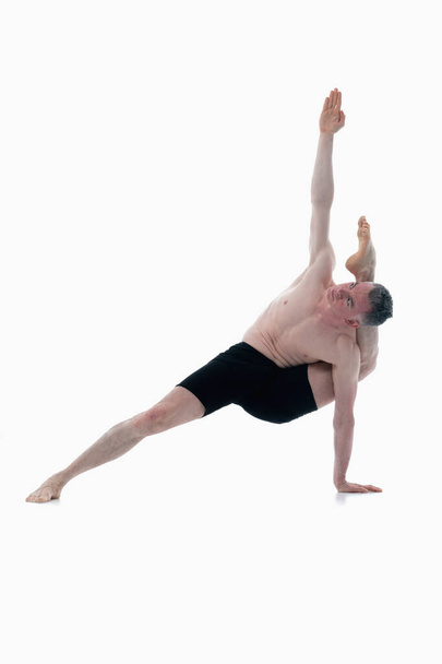 Kala Bhairavasana (Destroyer of the Universe Pose), Ashtanga yoga  Side view of man wearing sportswear doing Yoga exercise against white background. Vertical image. - 写真・画像