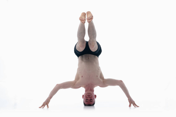 Headstand yoga asana, Ashtanga yoga Side view of man wearing sportswear doing Yoga oefening tegen witte achtergrond.  - Foto, afbeelding