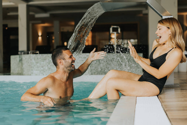 Hermosa pareja joven divirtiéndose en la piscina cubierta - Foto, Imagen