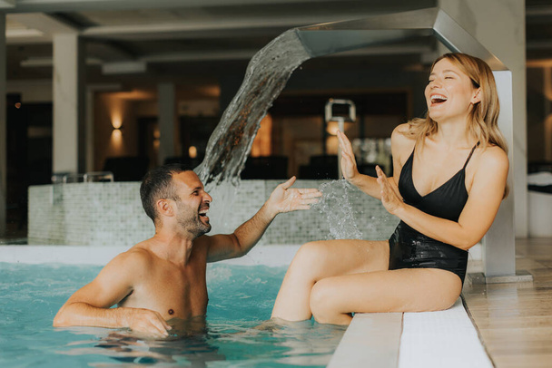 Handsome young couple having fun in the indoor swimming pool - Photo, Image