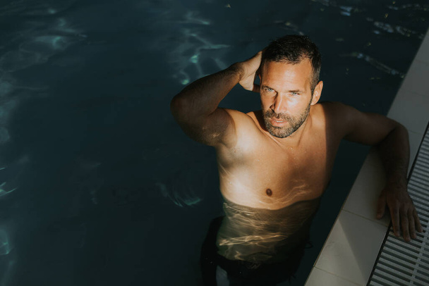 Hezký mladý muž relaxující na okraji krytého bazénu - Fotografie, Obrázek