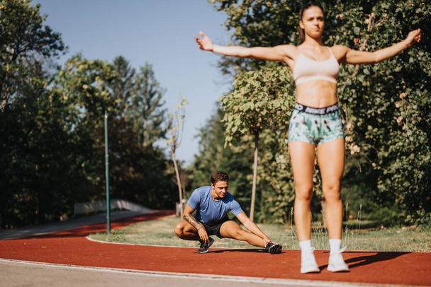 Kaukasisches Paar trainiert im Freien im Park, dehnt sich und wärmt sich auf. Sportlichkeit und Motivation führen zu positiven Ergebnissen für einen fitten Körper, einen gesunden Lebensstil. - Foto, Bild