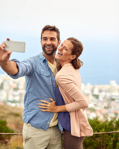 Paar, knuffel en selfie op vakantie, lachen en buiten op avontuur, liefde en herinneringen voor sociale media. Gelukkige mensen, smartphone en bonding of technologie, reizen en vakantie of gratis op datum. - Foto, afbeelding