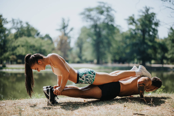 Caucasian couple exercises outdoors in a park, practicing push-ups and stretching. Their fit bodies and happy expressions reflect their commitment to a healthy lifestyle. - Fotografie, Obrázek