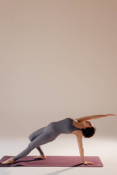 Junge schwangere Frau macht Yoga-Übungen und meditiert im Studio. Gesundheitsvorsorge, Achtsamkeit, Entspannung und Wellness-Konzept. - Foto, Bild