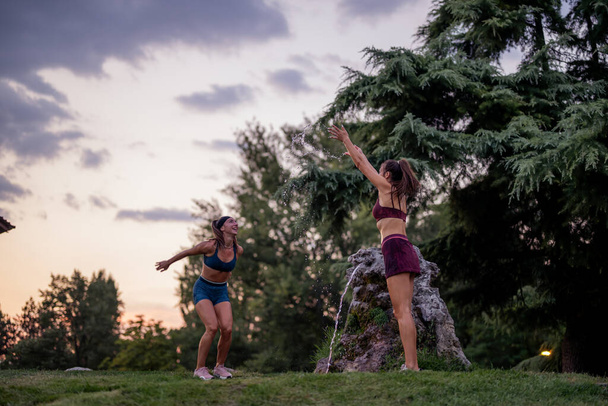 Mujeres felices disfrutando de momentos divertidos en el parque, salpicando agua y haciendo ejercicio al aire libre - Foto, imagen