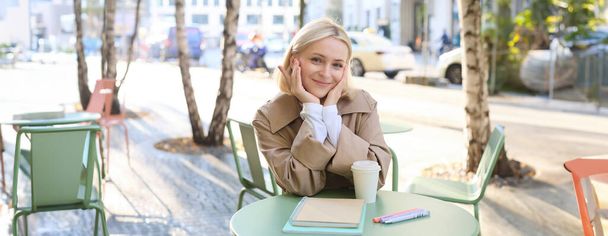 Porträt einer netten jungen Frau, Studentin, die sich im Café auf die Prüfung vorbereitet, Kaffee trinkt und studiert, Hausaufgaben macht. - Foto, Bild