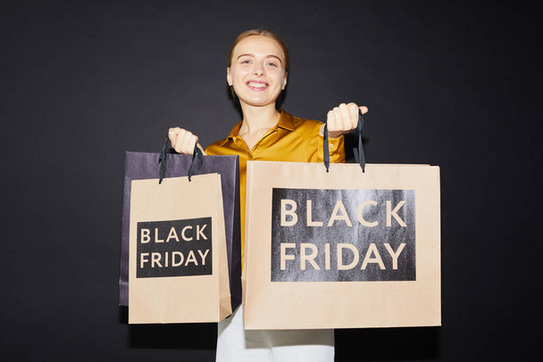 Smiling attractive young woman holding paper bags while being satisfied with best buy at Black friday - Foto, Bild