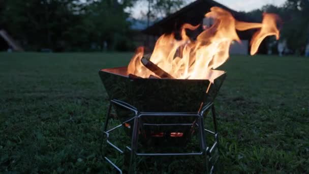 Помаранчеве полум'я піднімається з вогню в портативному металевому грилі на території кемпінгу в сутінках. Високоякісні 4k кадри - Кадри, відео