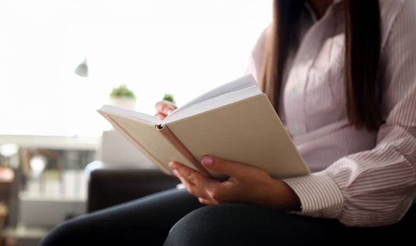 Female hand hold open book lying at couch closeup. Girl on sofa use datebook synopsis exam preparation delivery concept - Photo, Image