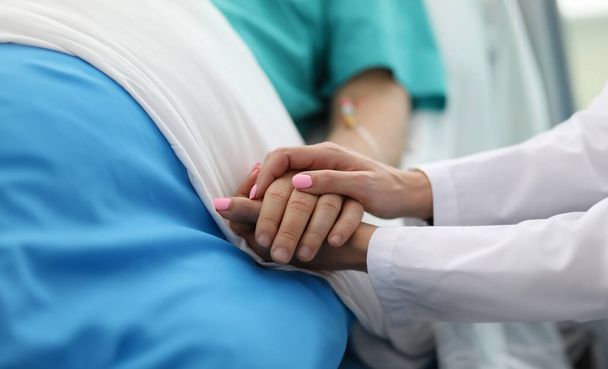 Close-up van mensen die elkaars hand vasthouden. Een vrouw die kalmeert voor een zieke patiënt in het ziekenhuis. Doc vraagt naar het welzijn van zieken. Begrip gezondheidszorg en geneeskunde - Foto, afbeelding
