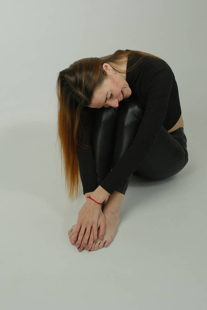 Retrato de una joven guapa con el pelo largo y rojo en pantalones negros y un suéter, posando en el estudio - Foto, Imagen
