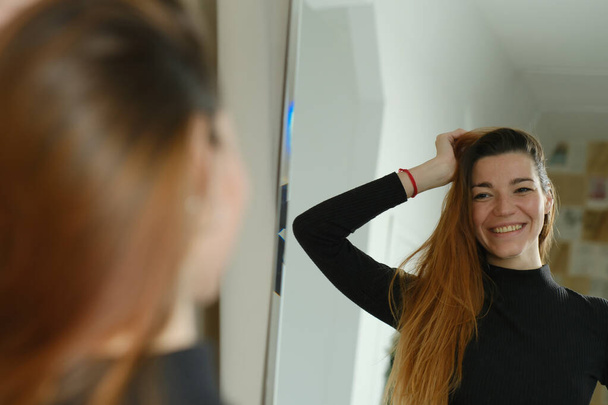 Портрет красивой девушки с веснушками и длинными рыжими волосами у зеркала в студии - Фото, изображение