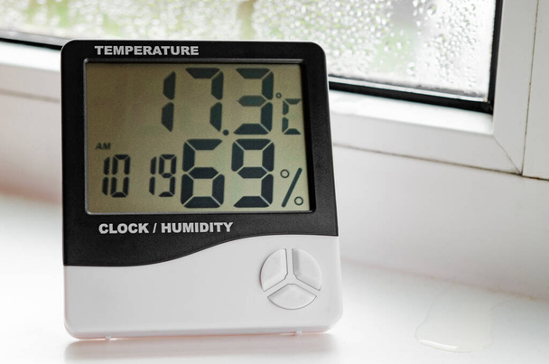Egy hőmérővel ellátott higrométer áll az ablakpárkányon páralecsapódással. Műanyag ablakok. - Fotó, kép