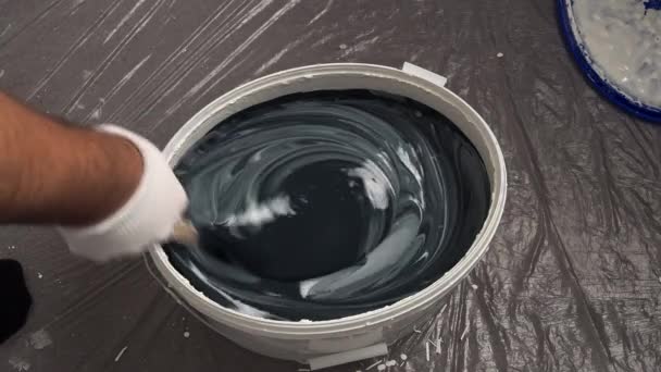 Egy munkás festéket kevert egy vödörbe, hogy fesse a falakat. Felkészülés a falak kifestésére. - Felvétel, videó