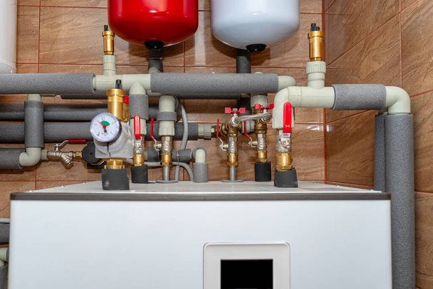 Una bomba de calor de aire moderna instalada en la sala de calderas de la casa, tubos y válvulas de plástico visibles. - Foto, imagen