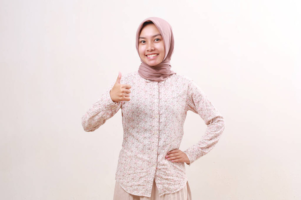 Boldog fiatal ázsiai muszlim nő áll, miközben mutatja elégedett kéz gesztus hüvelykujjal fel - Fotó, kép