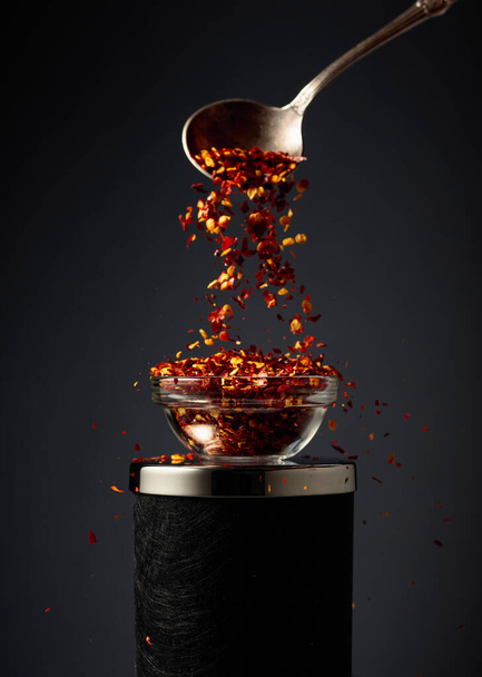 Flocos de pimenta vermelha quente são derramados em uma tigela de vidro pequena. - Foto, Imagem