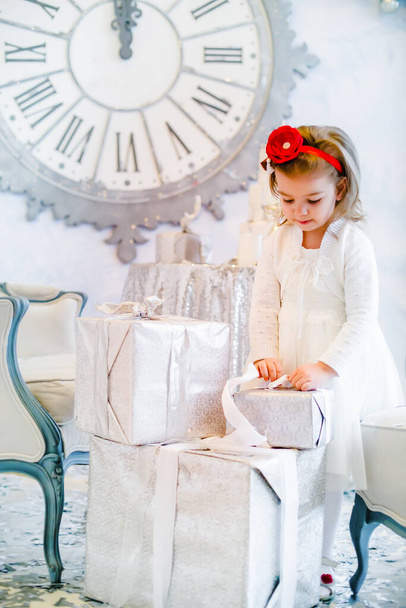 Χαριτωμένο κοριτσάκι σε ένα λευκό φόρεμα με ένα κουτί δώρου στο φόντο ενός χριστουγεννιάτικου δέντρου - Φωτογραφία, εικόνα