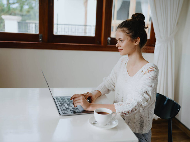 Креативна молода жінка працює за столом вдома в затишному інтер'єрі з чашкою напою, фрілансером домашнього офісу з посмішкою, спілкуванням та освітою онлайн. Високоякісна фотографія - Фото, зображення