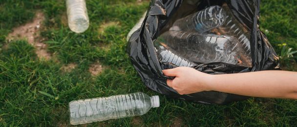 Lähellä käsi kerää roskat muovi puistossa. Vapaaehtoinen siivoamassa muovipulloa nurmikolla. Ympäristö, kierrätys ja suojelu. - Valokuva, kuva