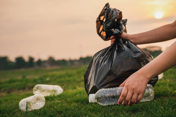 De cerca la mano recoge el plástico de la basura en el parque. Un voluntario limpiando una botella de plástico en un césped. Concepto de medio ambiente, reciclaje y protección. - Foto, imagen