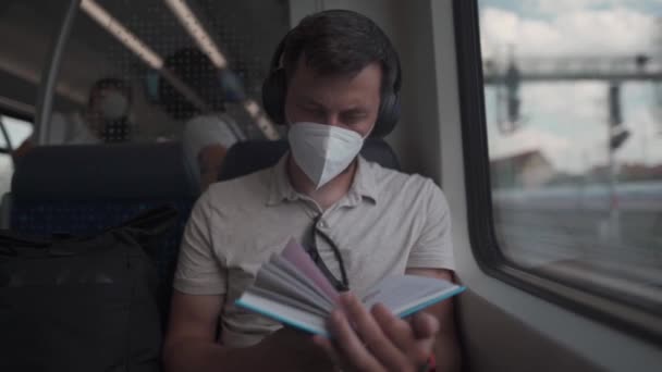 Een mannelijke passagier rijdt in de zomer in een Duitse voorstedelijke trein met een koptelefoon en leest een boek. Leerling leest handboek over draadloze oortelefoons tijdens het woon-werkverkeer op de trein. Dagelijks pendelen naar het onderwijs.  - Video