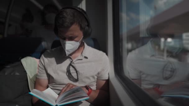 Пассажир, путешествующий на немецком поезде летом с беспроводными наушниками и книгой для чтения. Студент читает учебную тетрадь в беспроводных наушниках во время поездки в поезде. Ежедневно ездить в университет.  - Кадры, видео