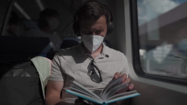 Um passageiro do sexo masculino monta um trem suburbano alemão no verão usando fones de ouvido e lendo um livro. Estudante lê livro didático sobre fones de ouvido sem fio durante o trajeto no trem. Viagem diária para a educação.  - Filmagem, Vídeo