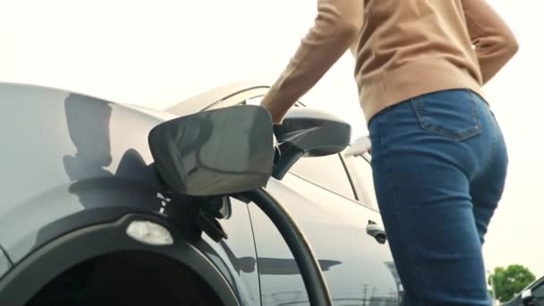 Azjatka jeżdżąca elektrycznym samochodem spędza wolny czas stojąc i relaksując się podczas zabawy smartfonem z łatwością czekając na naładowanie baterii w krótkim czasie. - Materiał filmowy, wideo