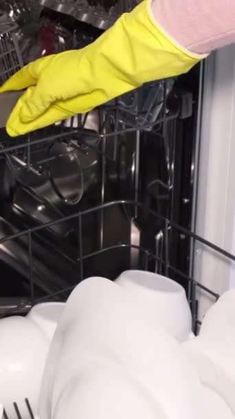 Close up view of female hand filling, inserting, loading dirty dishes, placing white plates into an open automatic built-in dishwasher. Housewife does her housework. Vertical video. - Footage, Video