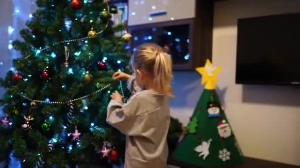 Klein meisje versiert de kerstboom met een krans van kralen. Hoge kwaliteit 4k beeldmateriaal - Video