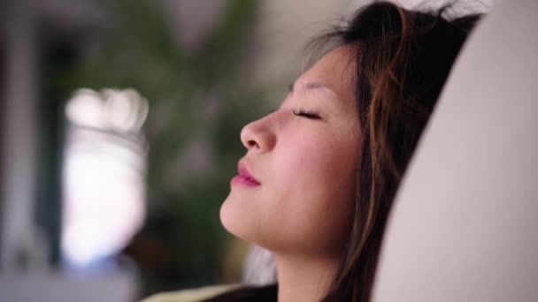 Крупним планом молода красива китаянка, що закриває очі, розслабляє дихання, сидячи на дивані. Азіатське покоління z гарненька дівчина відпочиває безтурботним, насолоджуючись вільним часом вдома. Жінка затишне домашнє життя, медитація. - Кадри, відео