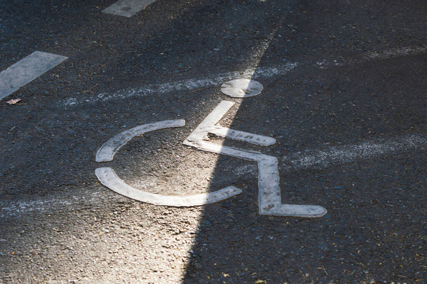 Biały znak dla wózków inwalidzkich na parkingu asfaltowanym, wskazujący zarezerwowane miejsce dla osób niepełnosprawnych fizycznie - Zdjęcie, obraz