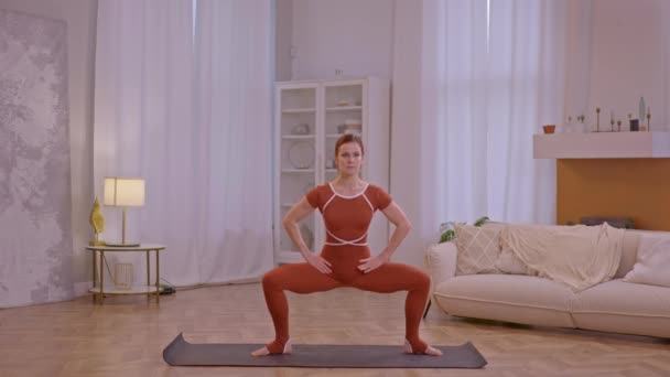 молода спортивна дівчина робить фізичну форму вдома, одягнена в коричневий комбінезон  - Кадри, відео