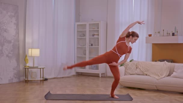 Молодая спортсменка занимается фитнесом дома, одетая в коричневый комбинезон  - Кадры, видео