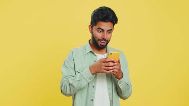 Szczęśliwy podekscytowany indyjski młody człowiek facet używać smartfona wpisując przeszukiwanie krzycząc powiedzieć wow tak okazało się wielkie zwycięstwo dobra wiadomość cel loterii osiągnięcie świętując sukces, wygrywając grę na żółty - Materiał filmowy, wideo