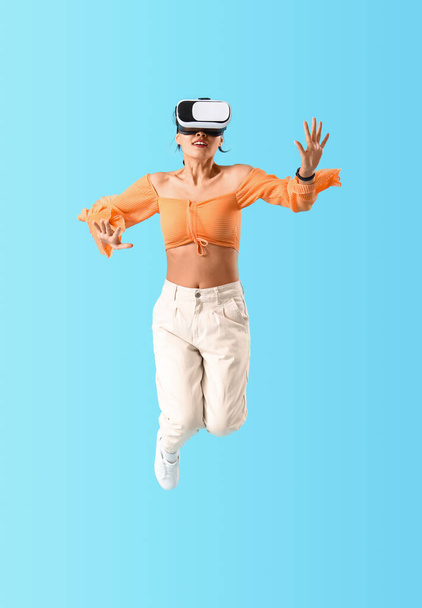 Mujer joven saltando con gafas VR sobre fondo azul - Foto, Imagen