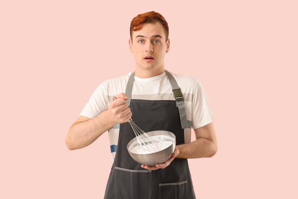 Pastelero masculino con bol y batidor preparando sabroso merengue sobre fondo rosa - Foto, imagen