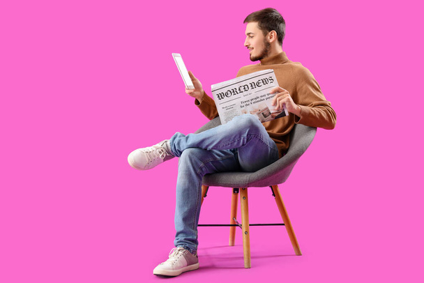 Jongeman met krant en tablet computer in fauteuil op paarse achtergrond - Foto, afbeelding