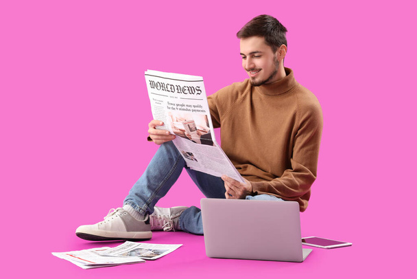 Young man with newspaper and laptop sitting on purple background - Photo, Image